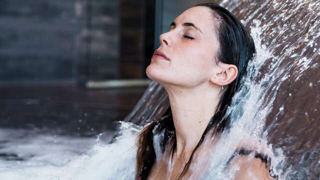 Donna che riceve un massaggio ad acqua pressurizzata sulla schiena sotto la cascata di una piscina termale.